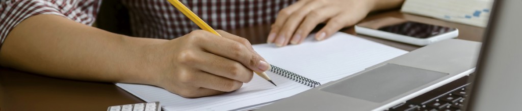 A woman's hands writing on a lined paper notebook